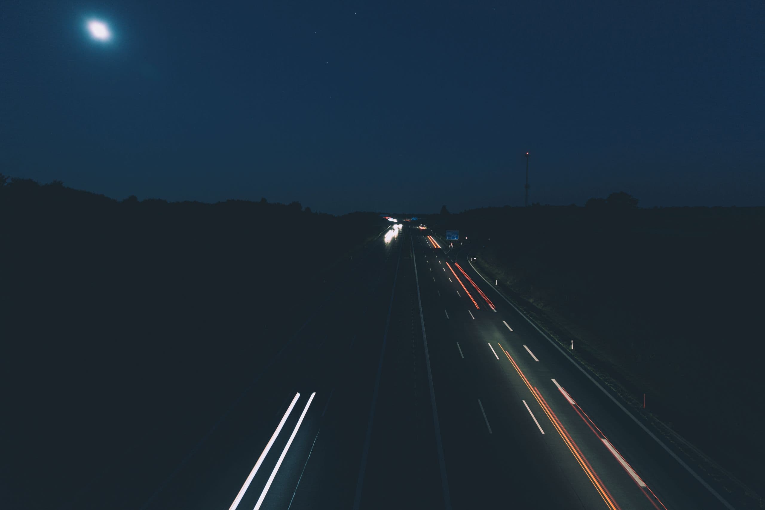 A highway at night under a full moon, headlights drawn into lines